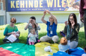 Several women sit in a circle with babies playing a hand game
