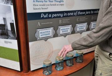 View of a text panel with four glass jars and someones hand touching the lid of one of the jars. 