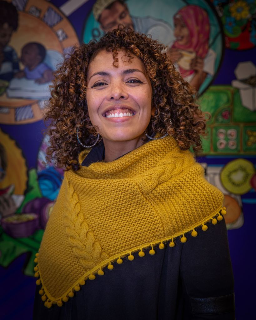 A person posing and smiling in front of a vibrant mural