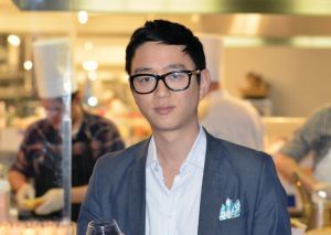 Headshot of Peter Kim with chefs seen blurred in the background.