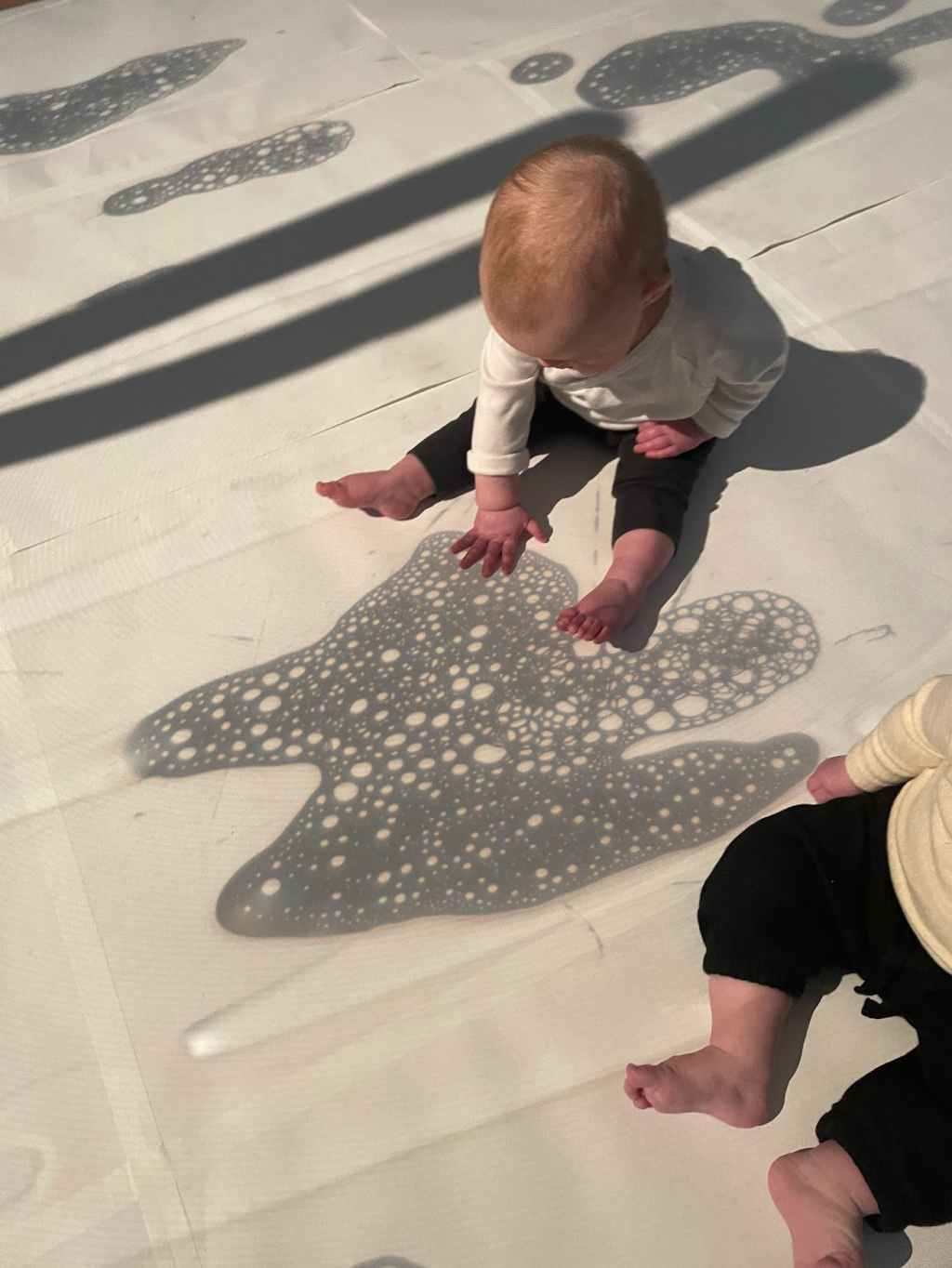 A baby explores and interacts with a shadow projection on the ground