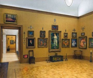 Multiple paintings and portraits hang in a light brown room.