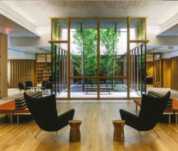 Two black chairs face a garden with small trees surrounded by glass.
