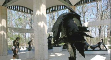 Multiple modern statues stand in a white covered pavilion.