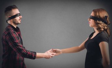 A blindfolded man and woman reach to shake hands with each other. This represents an unbiased hiring process.