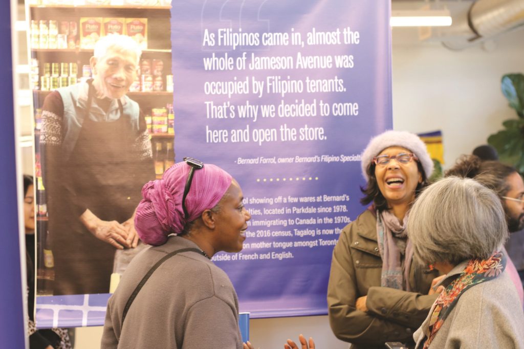 Several women stand smiling and laughing in front of an exhibition banner.