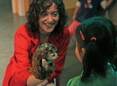 A woman is showing a child a hedgehog puppet. 