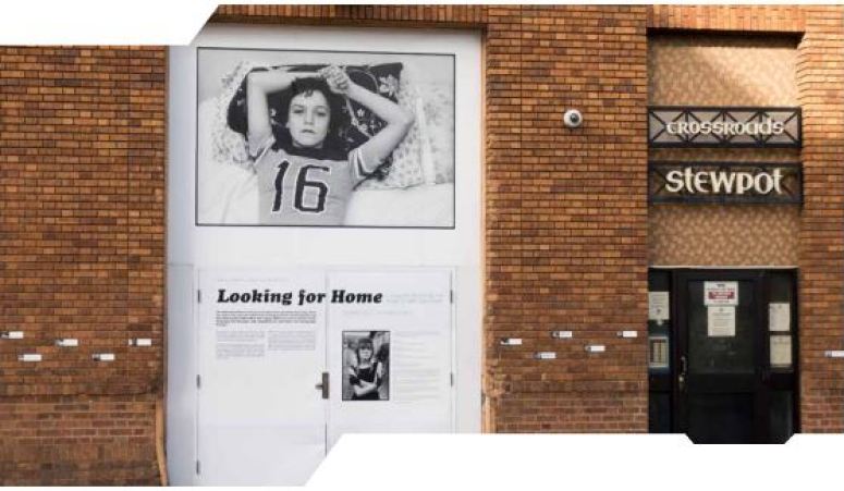 View of a brick wall with several text and image panels showing various people experiencing homelessness. 