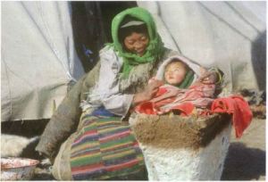A mother holds her baby in a papoose next to her side.