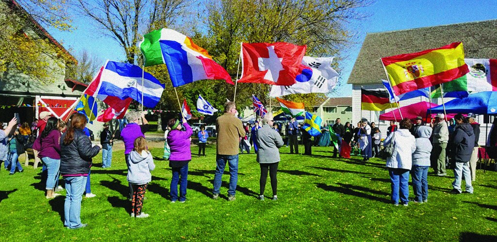 A group of people stand outside in a green grassy area carrying different colorful flags.