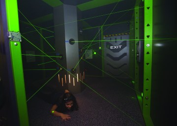 A young woman slides on her stomach under green lasers.