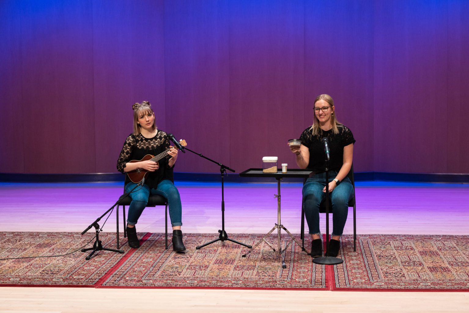 Two people on a stage with microphones playing instruments