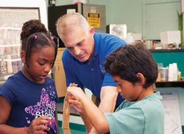 David Wolf shown helping two young children (a black girl and a brown boy) work on a piece of art.