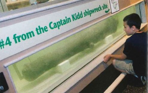 A young man looks into a tank filled with water looking at the barrel of a cannon can be seeen in the water.