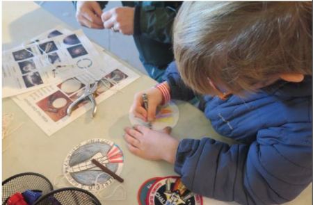 A young boy works on a project with other children nearby.