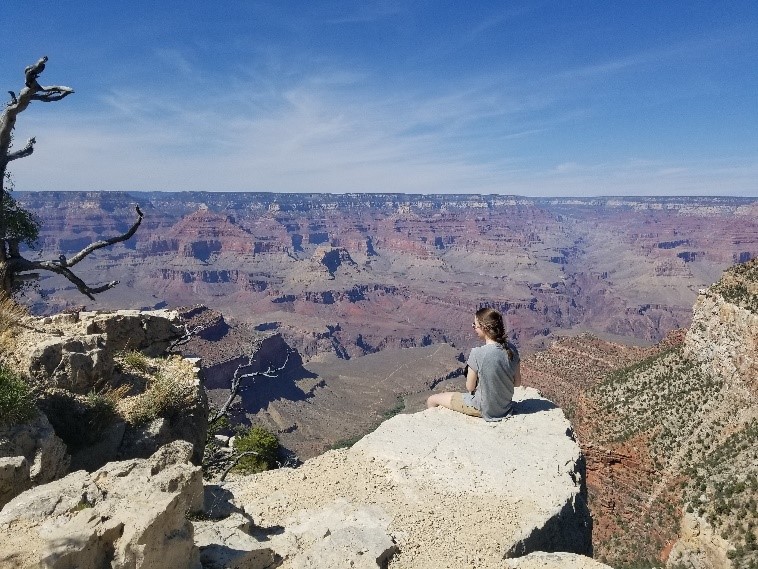 A woman sits on a rock ledge overlooking the Grand Canyon.