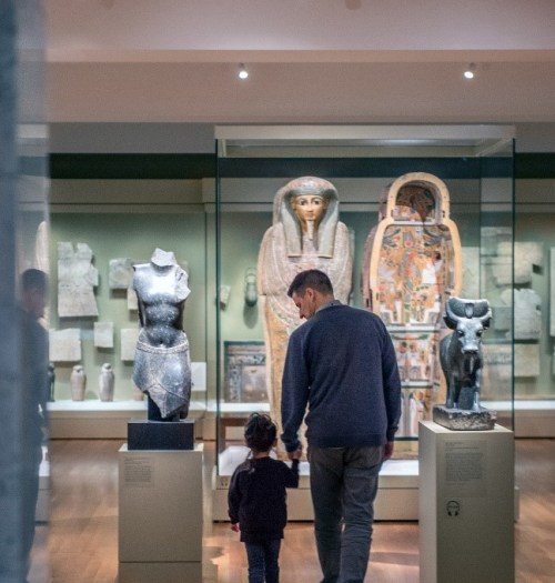 An adult and child tour a gallery of Ancient Egyptian artifacts.