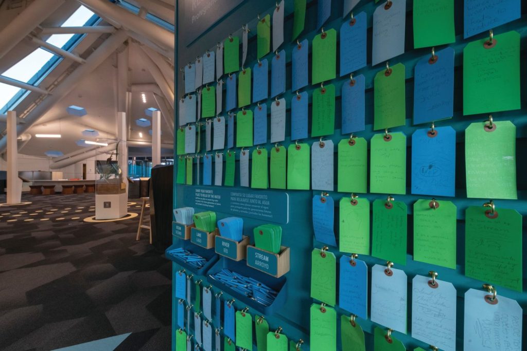 A colorful wall with push pin strips of paper where visitors can share their thoughts. 