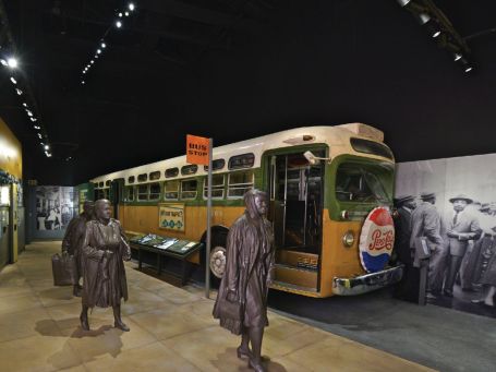 Image of a buss with grey statues in front inside an exhibition.