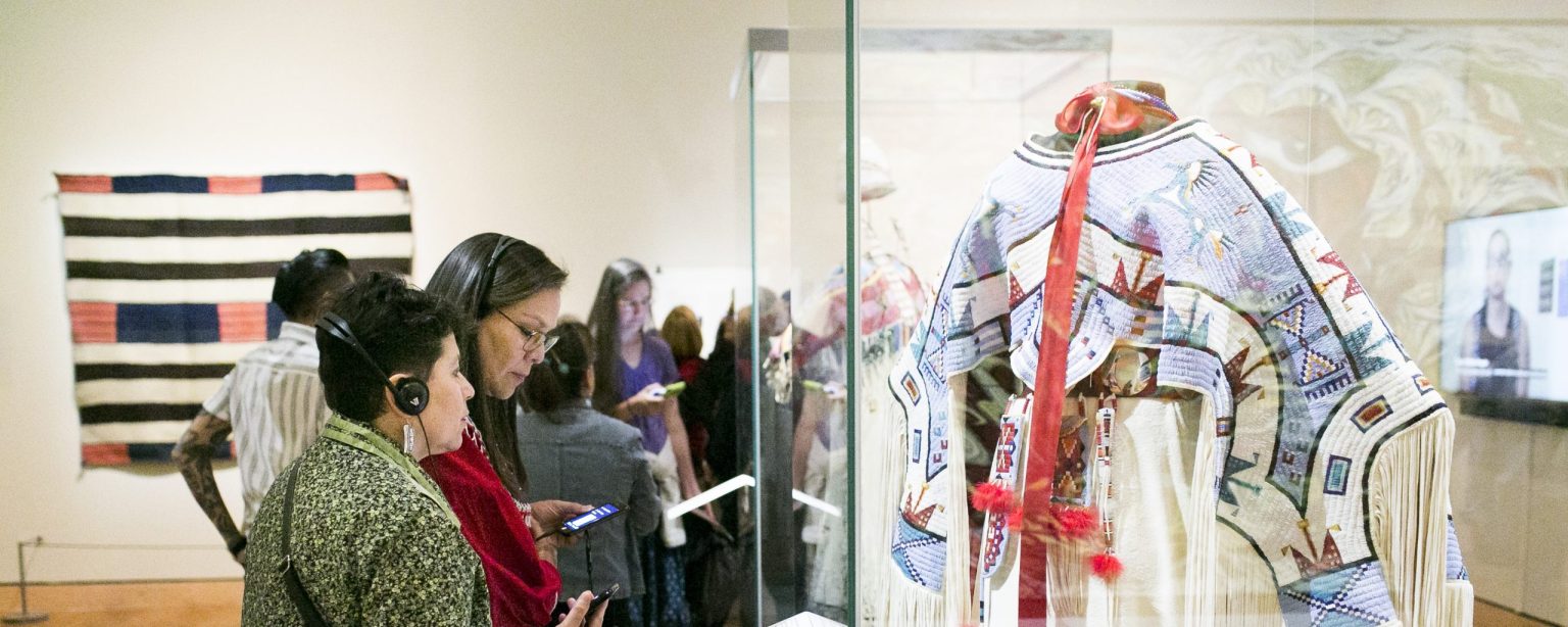 Visitors look at clothing, textiles, and video interviews displayed in galleries