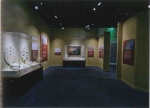 View looking into a museum gallery with wall cases and dark blue carpeting.