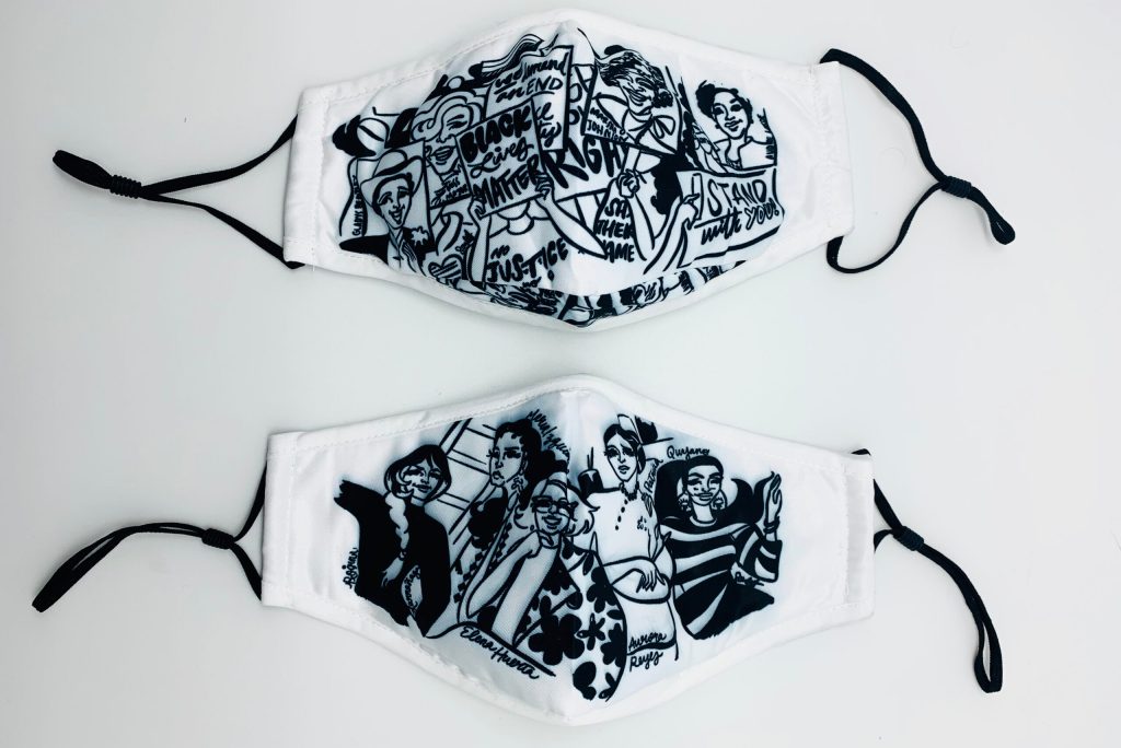 Two white masks with black cartoon-style designs on them, one showing activities holding signs with messages like "Black Lives Matter" and another showing a group of women posing.