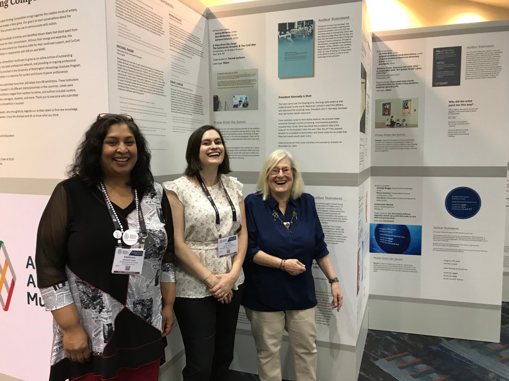 Three people posing in front of posters on display.