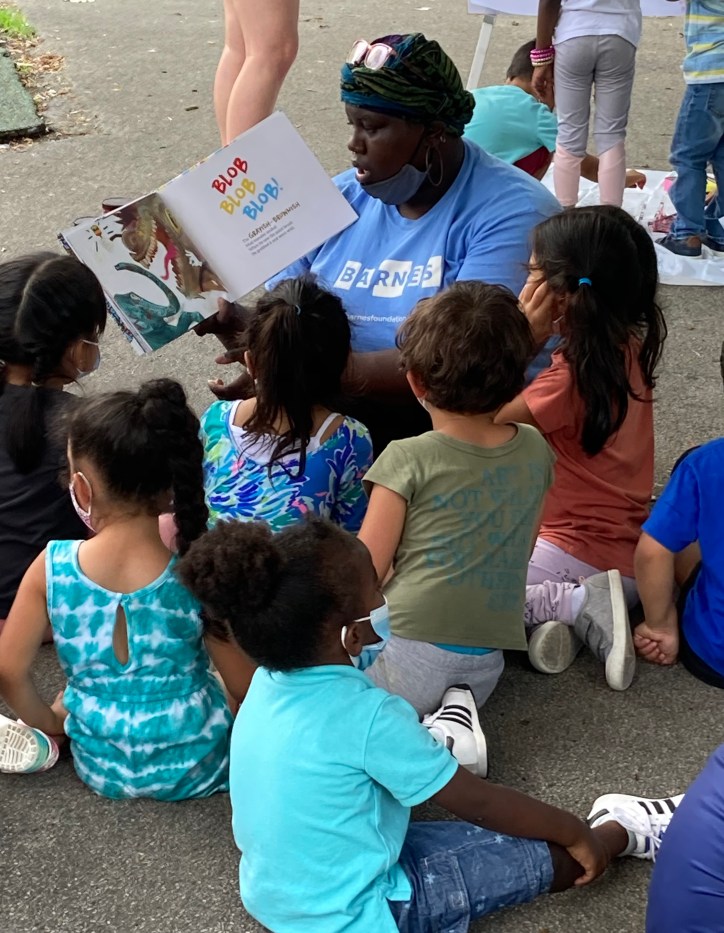 An educator wearing a Barnes t-shirt reading from a book to a group of children