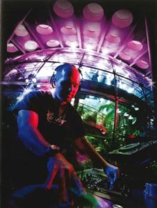 A man stands spinning records in a glass enclosed space. Taken with a fisheye lens.