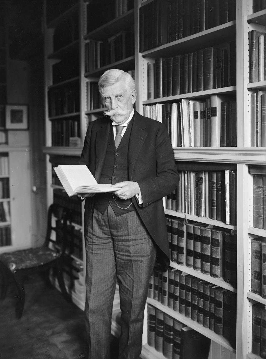 A black-and-white portrait of Oliver Wendell Holmes standing in a library and holding a book.