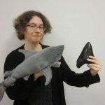 Image of Karen Malone holding a shark puppet "Reggie" and real shark tooth