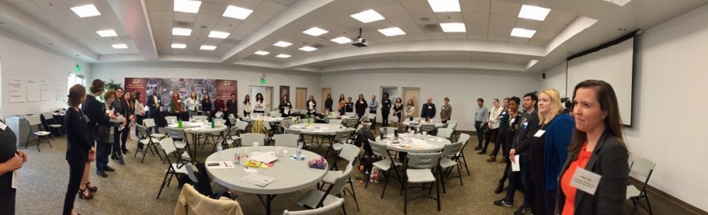 A panoramic shot of a meeting room with round tables and a group of people standing around the perimeter.