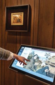 Image of someone's arm pointing at an angled interactive screen with a drawing of two figures on it.