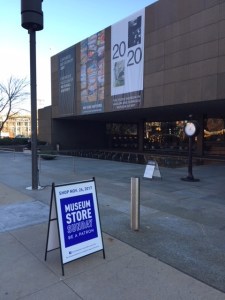 View looking at the exterior of the Carnegie Museum of Art with a sandwich board sign standing on the sidewalk that says "Shop Nov. 26, 2017 - Museum Store Sunday Be a Patron"