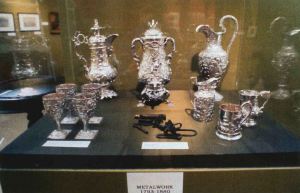 Display case with a pair of slave shackles and silver vessels in Metalwork 1793-1880.