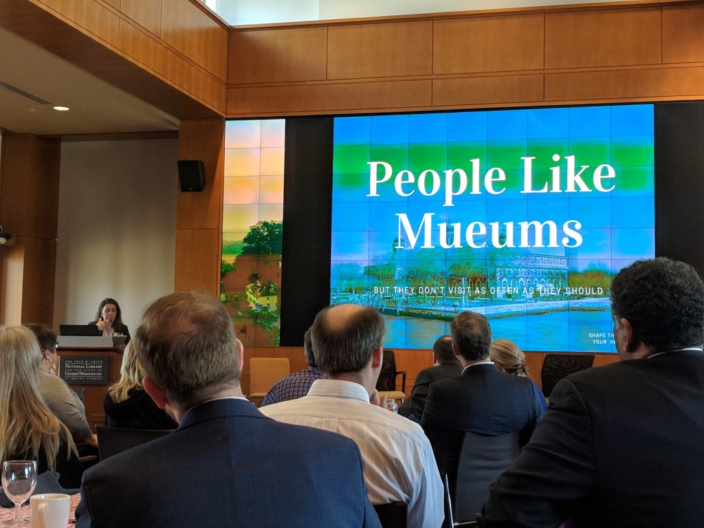 View of the conference room where the historic house summit was held with a group of mainly men looking at a screen with "People Like Mueums" displayed on it.