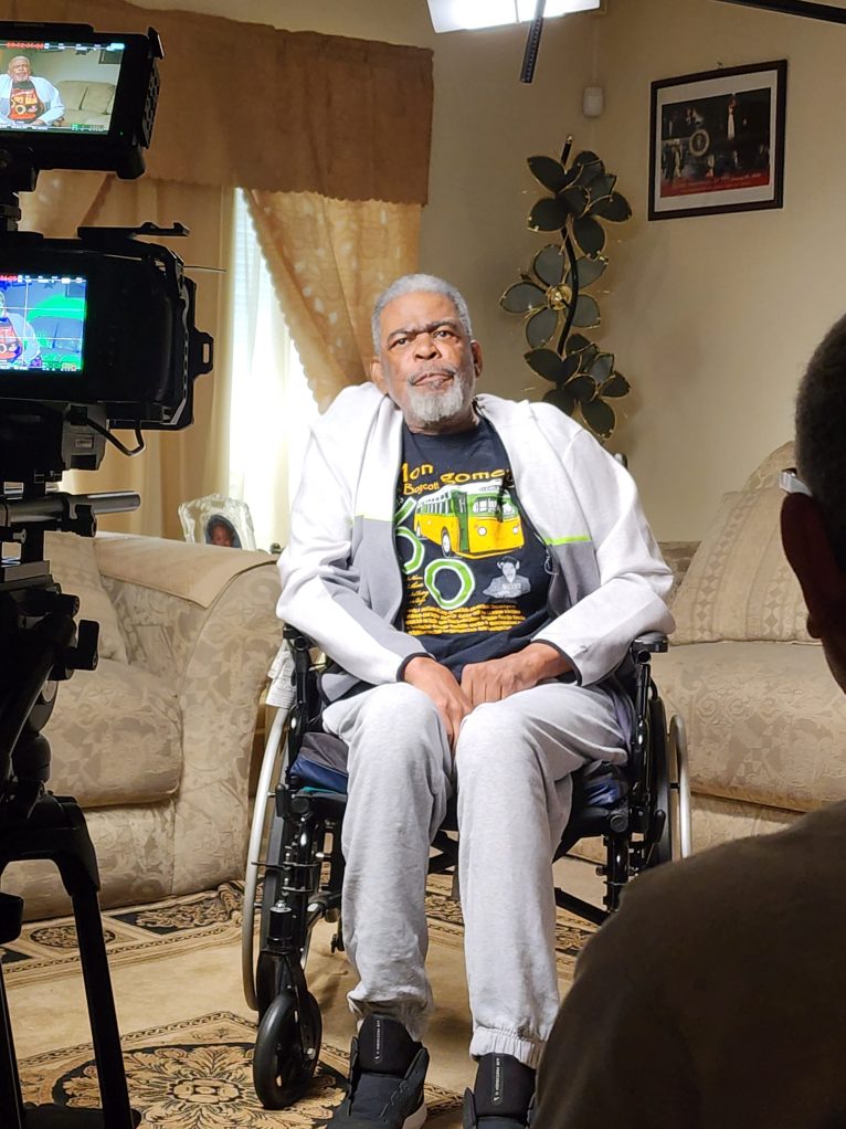 An interview subject seating in a wheelchair wearing a t-shirt commemorating the sixtieth anniversary of the Montgomery bus boycott
