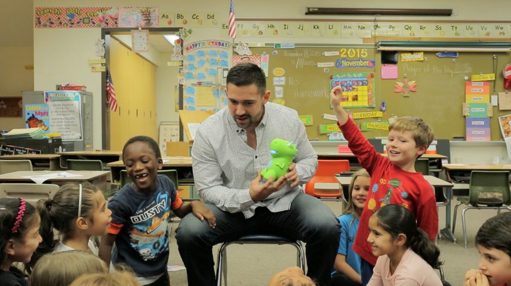 A man sits with a group of children holding a green dinosaur