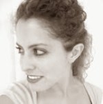 Black and white image of a woman looks to her right with curly brown hair pulled back wearing a light colored top. 