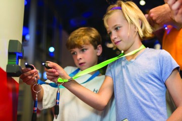 Two young children hold lanyards up to a key entrance to an exhibit. 