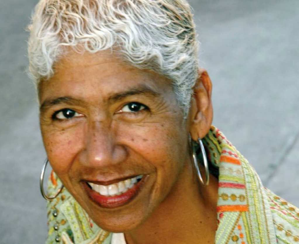 A headshot of Ericka Huggins wearing a green and orange patterned blouse