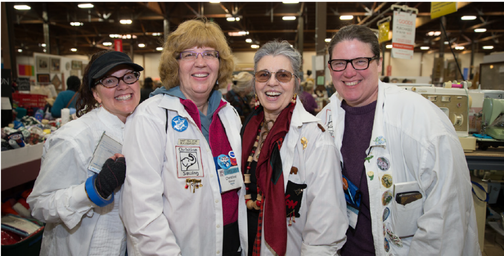 A group of four women each wearing a white lab coat smile at the camera.