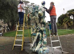 Two conservators clean a ceramic sculpture in a courtyard