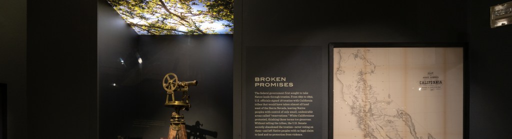 A view of the "Broken Promises" section, with a land-surveying tool, a map of the state of California, and several framed documents visible.