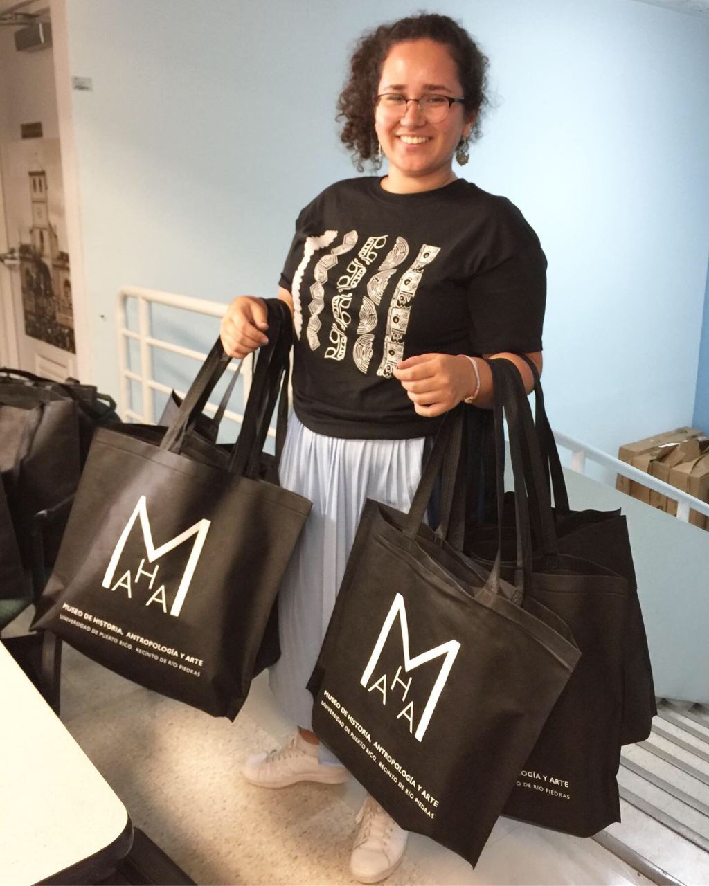 The intern stands with two armfuls of empty tote bags waiting to be filled.