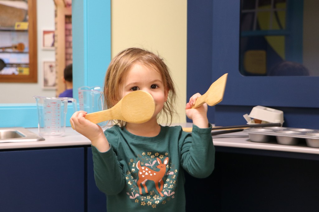 A young child playing with wooden spoons