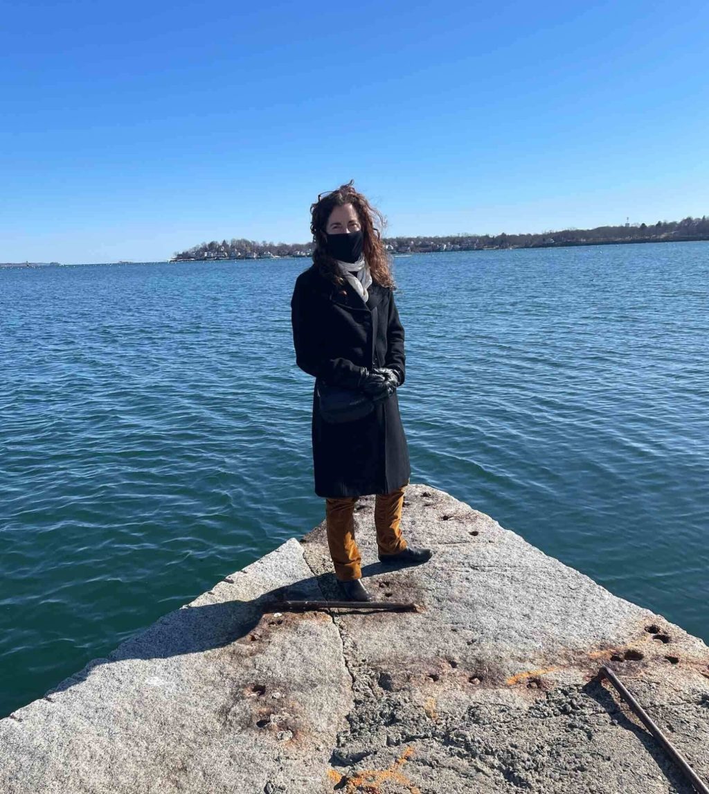 A person standing on a rock near a body of water wearing a coat and mask