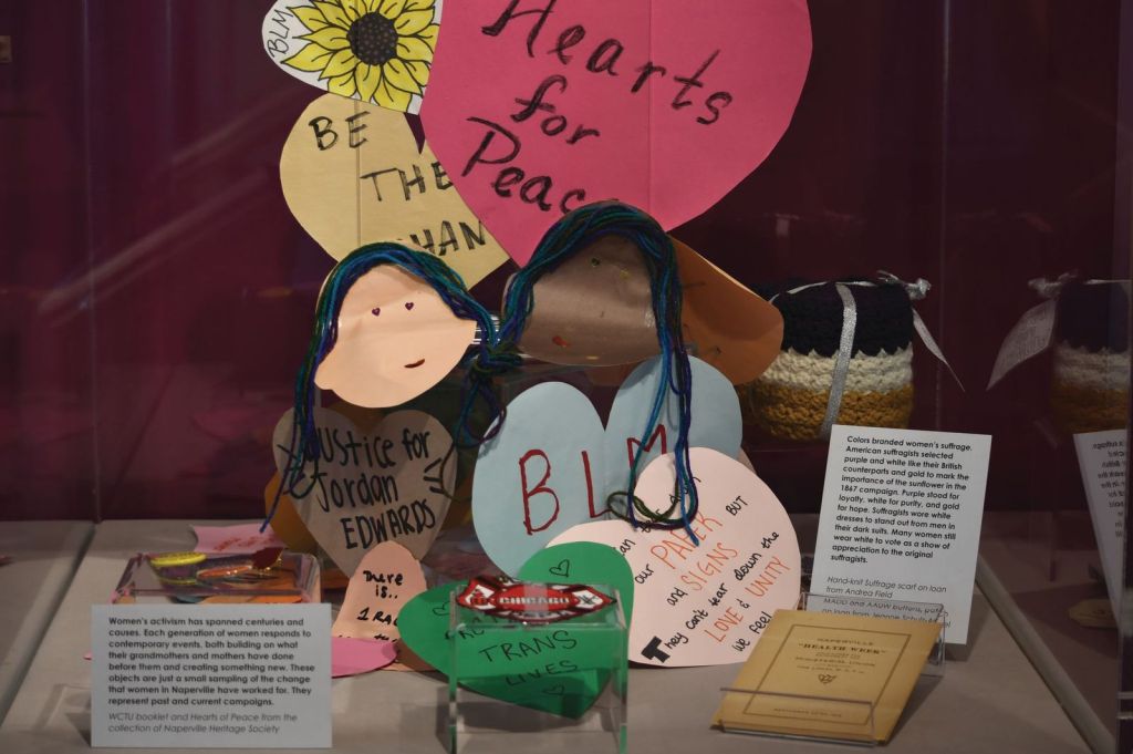 A group of handmade paper art in the shape of hearts sits on a shelf with an interpretive label.