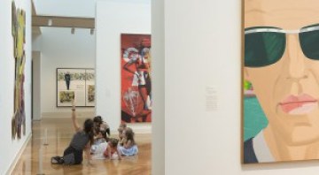 Several people sit on the floor of a gallery and look up at the art.
