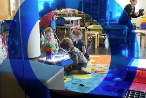 Picture taken through a blue tinted glass looking toward a group of children interacting with a light table.